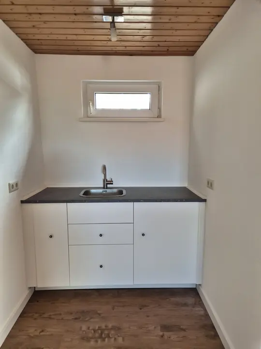 White kitchenette with sink under a small window and wooden ceiling