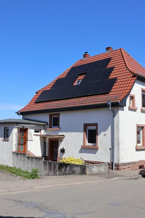 Street view of the white house with red sandstone window frames, red tile roof and solar panels